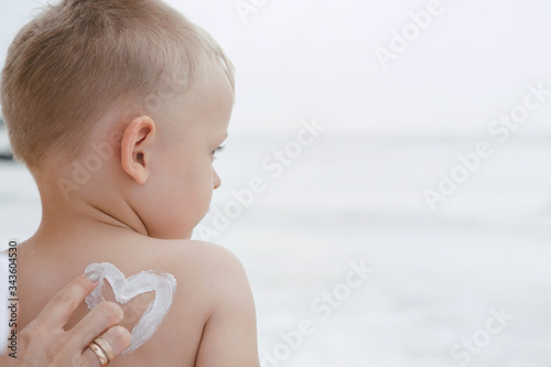 a protective cream on a baby. Mother lubricates her son with cream on vacation near the sea.