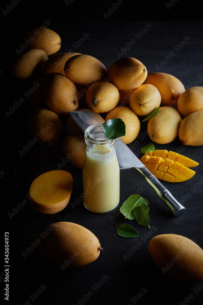 fresh organic mango smoothie in a glass bottle among ripe Thai mango fruits on a dark background, mango shake, detox drink, vertical banner fresh organic mango smoothie in a glass bottle among ripe Thai mango fruits on a dark background, mango shake, detox drink, vertical banner