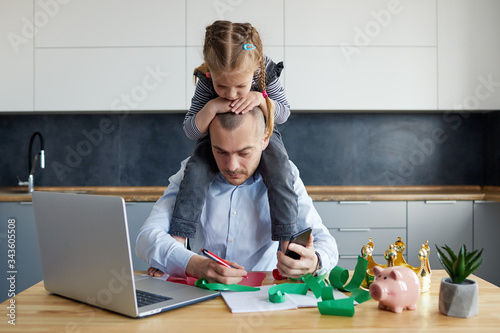 Father Working from home on laptop during quarantine. Little child girl make noise and distracts father from work on the kitchen office