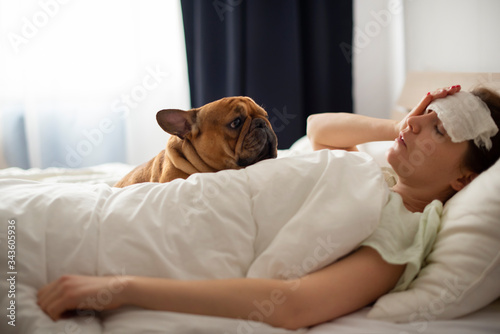 A young girl is lying in bed with heat, her French bulldog is helping her. Coronovirus patient