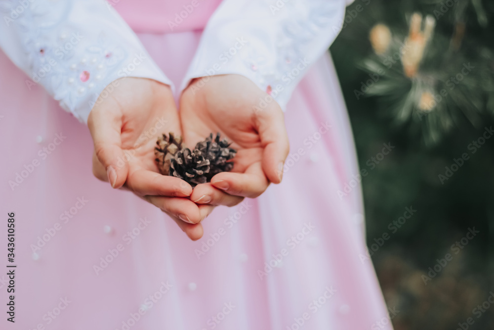 The girl in a pink dress holds cones in the hands of the forest