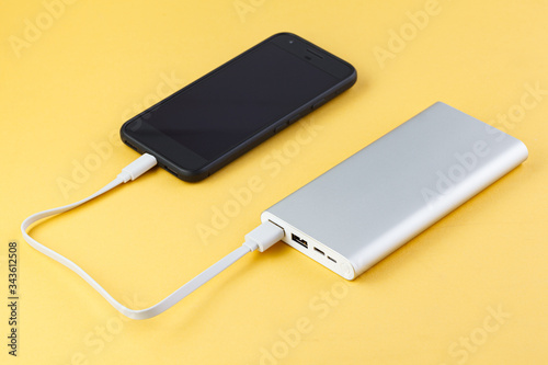 Power bank charges your smartphone on yellow background. Universal external battery for gadgets. Power bank for charging mobile devices. External battery for mobile devices.