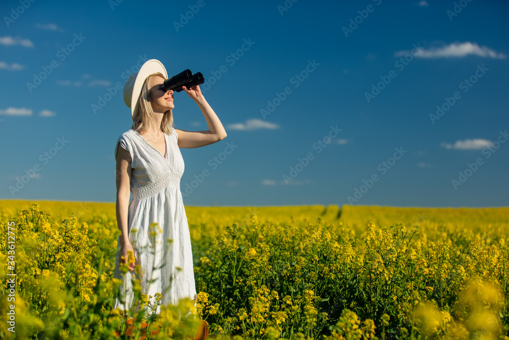Fototapeta premium Beautiful woman in dress with binoculars in rapeseed field