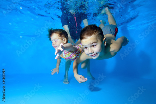 Two children, a small boy and a girl, are engaged in swimming in a children's pool. They play and dive under the water with their eyes open, and a female instructor helps them. Close up. Concept.