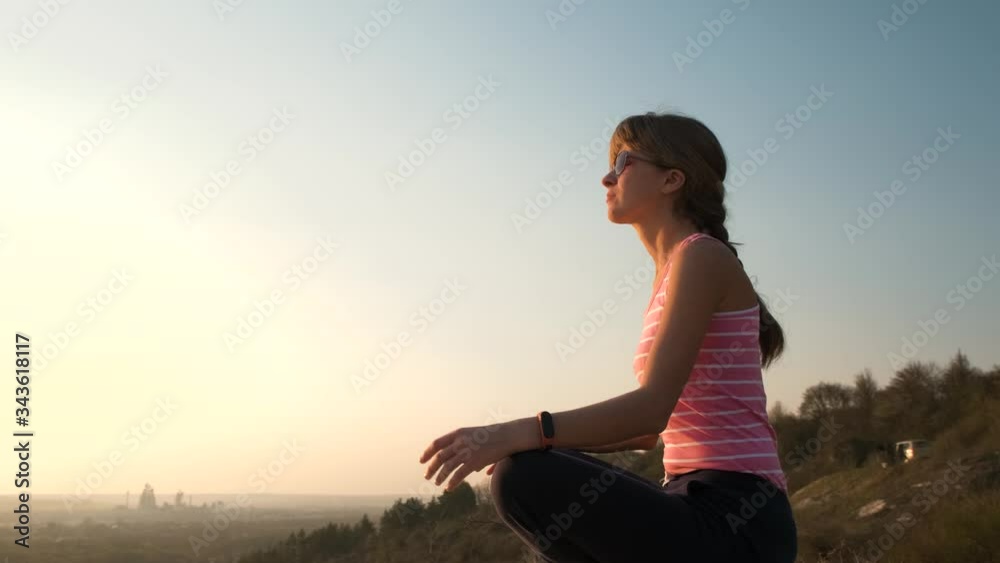 Young relaxed woman sitting outdoors on a big stone enjoying warm summer day. Girl meditating and relaxing on nature at sunset.
Young relaxed woman sitting outdoors on a big stone enjoying warm summer day. Girl meditating and relaxing on nature at sunset.