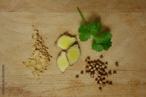 Ginger root and powder and coriander fruits and leaves on wooden trencher photo