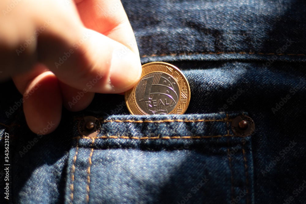 Dedo segurando uma moeda de 1 real brasileira no bolso da calça jeans azul  masculina - Empobrecimento da População - Moeda desvalorizada Stock Photo |  Adobe Stock