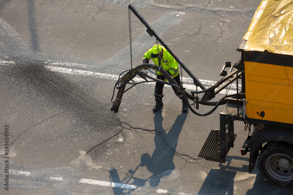 Road surface restoration work. The worker performs on road patcher work on the repair of cracks by filling and sealing with coated by bitumen emulsion and dry aggregate in the asphalt surface.