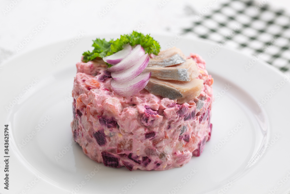 Russian salad herring under a fur coat. It is made from potatoes, carrots, beets, herring, onions. On a white plate, close up. Russian salad herring under a fur coat. It is made from potatoes, carrots, beets, herring, onions. On a white plate, close up.