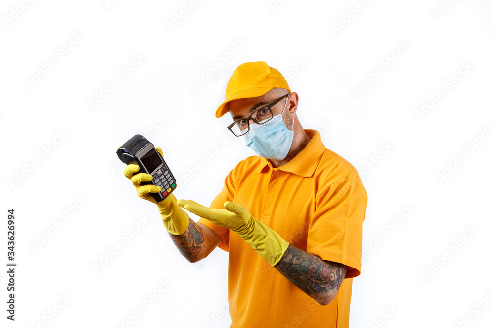 A cautious young man from a courier delivery service in a medical mask and gloves holds a terminal in his hands for cashless payment on a white background A cautious young man from a courier delivery service in a medical mask and gloves holds a terminal in his hands for cashless payment on a white background