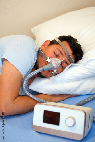 Healthy young man wearing nasal mask and using Cpap machine for sleeping smoothly all night long on his left side cross arms without snoring. sleep apnea therapy. selective focus.