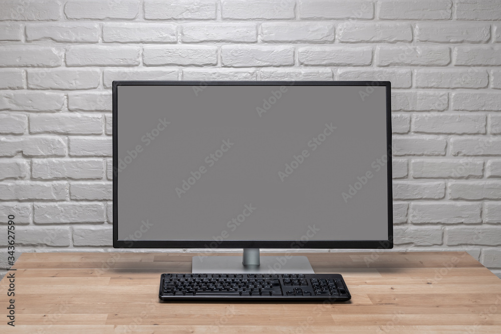 Fototapeta premium Blank screen computer monitor on working desk with brick wall