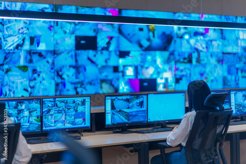Group of Security data center operators (administrators) working in a group at a CCTV monitoring room while looking at multiple monitors ( computer screens) photo
