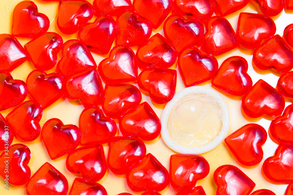 condom and many small glass red hearts yellow background, protected sex concept, sex for love between lovers, reflection in glass condom and many small glass red hearts yellow background, protected sex concept, sex for love between lovers, reflection in glass