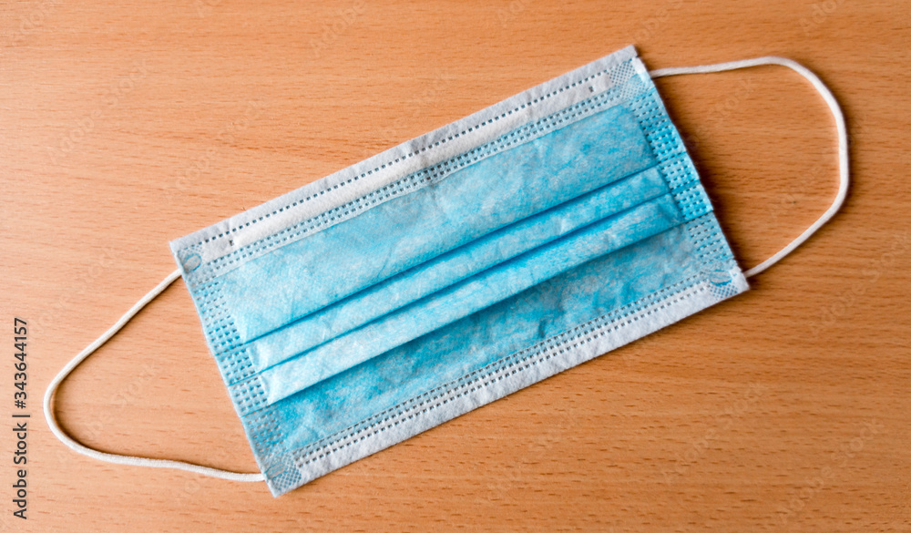 Blue medical mask lies on a wooden background. Coronavirus epidemic concept Blue medical mask lies on a wooden background. Coronavirus epidemic concept