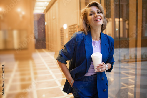 Stylish business lady on lunch break while working out of office. Fahionable female manager drinks cappuccino from a paper cup.. photo