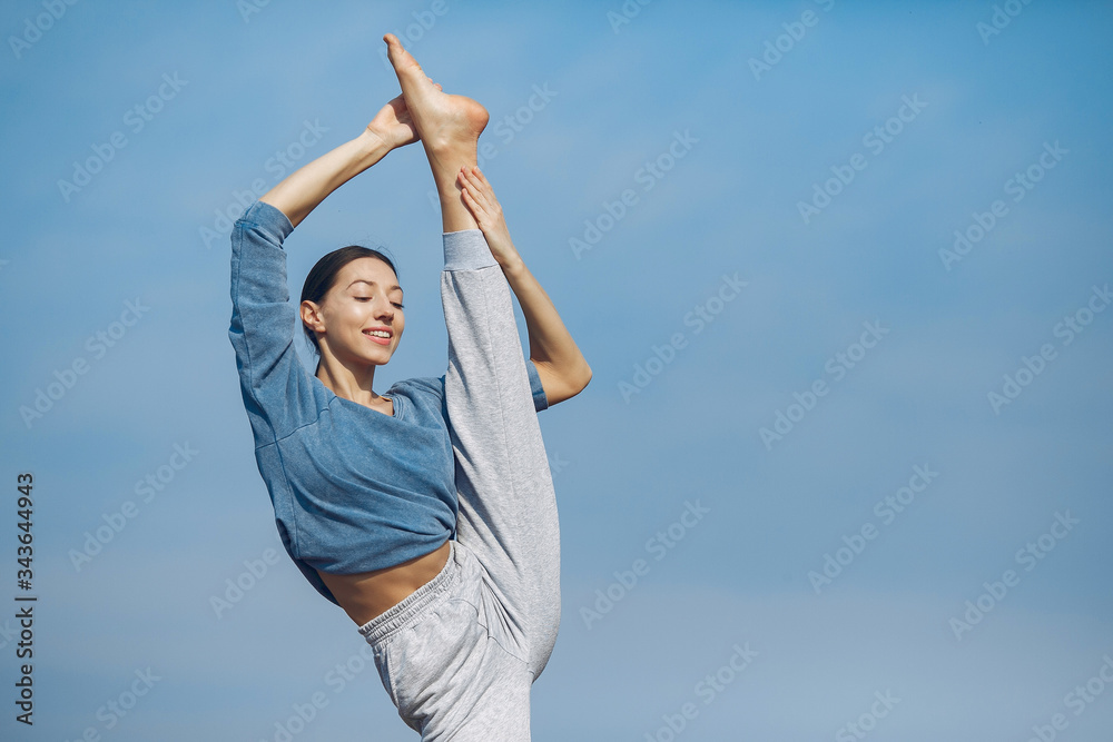 Beautiful girl training on a sky background. Woman in a blue sweater. Lady make a yoga Beautiful girl training on a sky background. Woman in a blue sweater. Lady make a yoga
