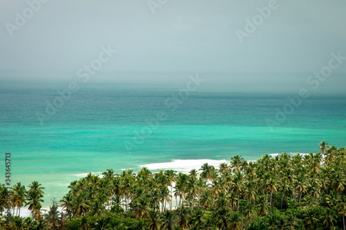 Beach landscape with sand, white foam waves, palm trees, blue sky, turquoise water and clouds, paradise Caribbean coast of Dominican republic 