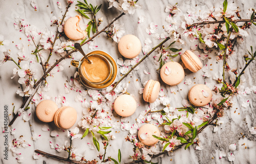 Flat-lay of cup of hot espresso offee, sweet macaron cookies, white spring blossom flowers and white marble background, top view © sonyakamoz