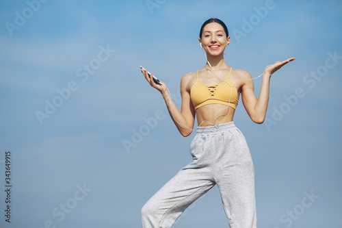 Beautiful girl standing on a sky background. Woman in a yellow top. Lady with phone in her hands © prostooleh