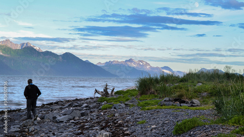 Person walking along rocky beach shoreline in Alaska mountain landscape background. Alaska tourism in the summer