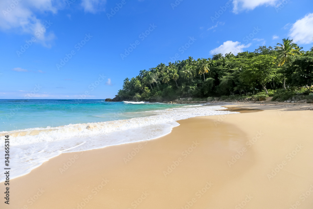 Beach landscape with sand, white foam waves, palm trees, blue sky, turquoise water and clouds, paradise Caribbean coast of Dominican republic 