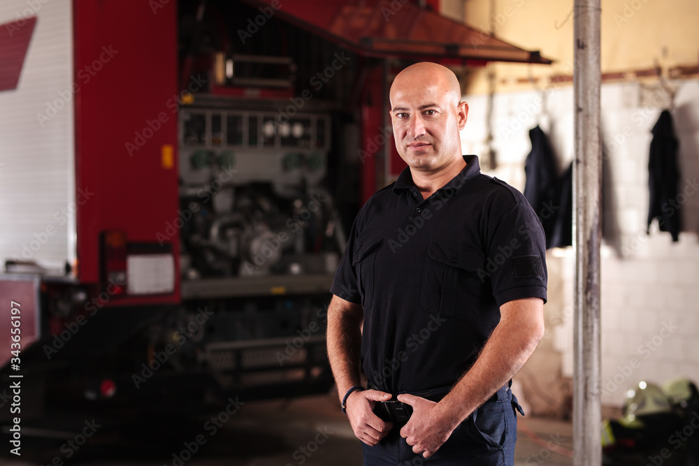Professional fireman portrait. Firefighter wearing uniform of shirt and trousers. Fire truck in the background.