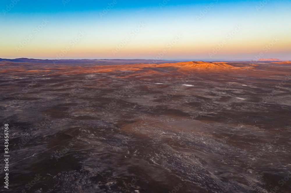 Obraz premium Aerial view of Andes mountains with orange tones from the sunset exploring Atacama Desert vast dry extensions. An awe road trip adventure crossing the infinite sand extensions of this amazing dry land