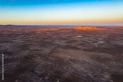 Aerial view of Andes mountains with orange tones from the sunset exploring Atacama Desert vast dry extensions. An awe road trip adventure crossing the infinite sand extensions of this amazing dry land