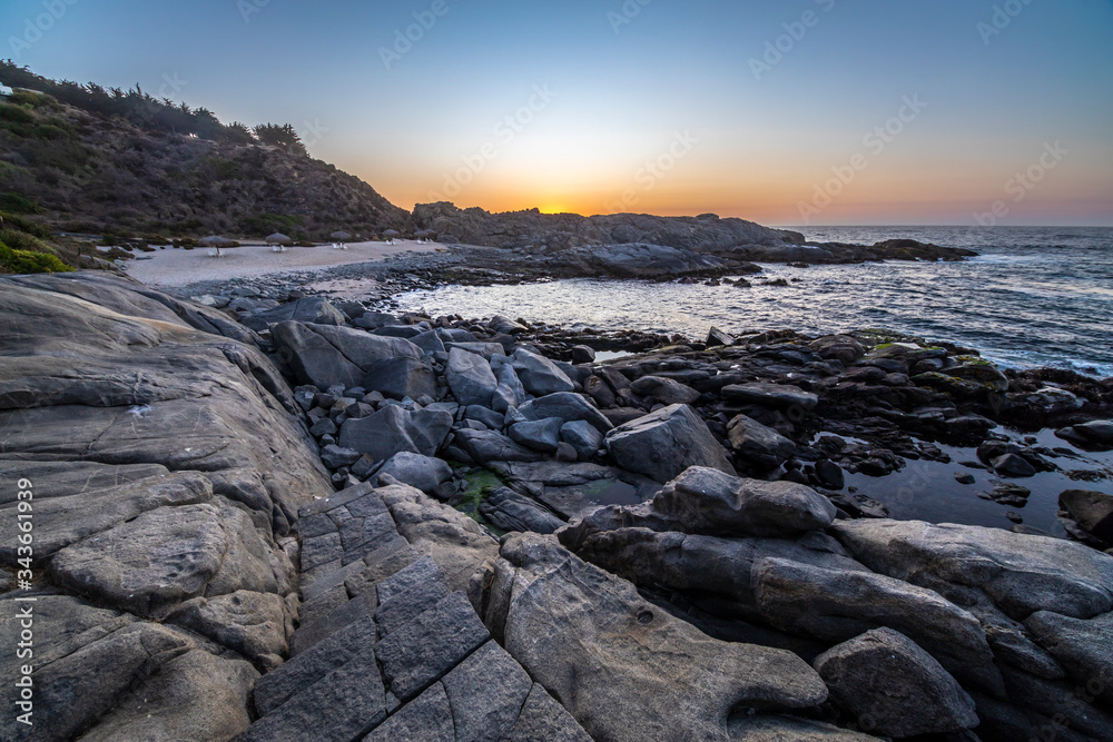 Amazing view of the sunset over the water in the Chilean coast. An idyllic scenery with the sunlight illuminating the stone pavement with orange tones and the sea in the background under a moody sky
