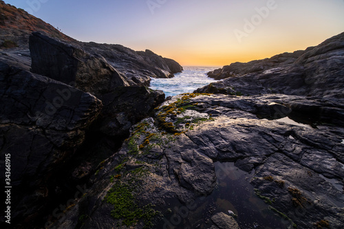 An amazing view of the sunset over the water in the Chilean coast. An idyllic beach scenery with the sunlight illuminating the rocks with orange tones and the sea in the background under a moody sky 