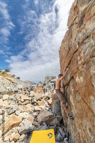 Male rock climber practicing bouldering without rope on a boulder area in front of the sea. A high boulder for people with tenacity and confidence to climb the cliff with the risk of severe damage 