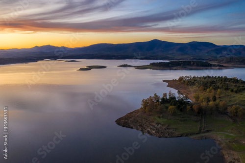 Aerial view of Gabriel y Galan lake at Extremadura countryside. An amazing view during sunset time on a cloudy day. The colors of the sky reflected over the lake waters give an idyllic landscape view 