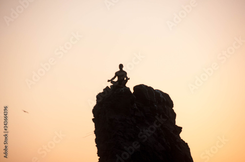 A man meditating on top of a big rock at sunset