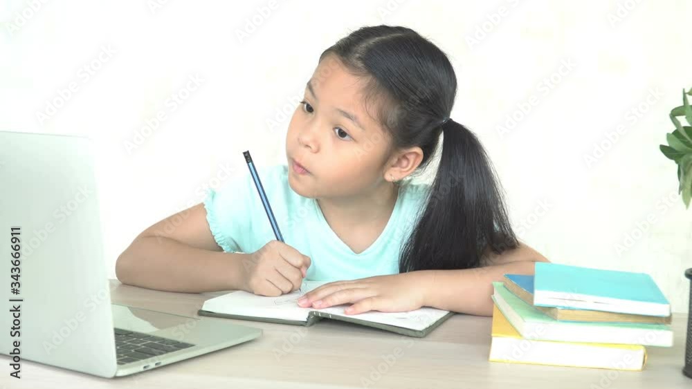 Asian kid schoolgirl studying homework math during her online with laptop lesson at home, social distance during quarantine, self-isolation, online education digital technology concept, home schooler. Asian kid schoolgirl studying homework math during her online with laptop lesson at home, social distance during quarantine, self-isolation, online education digital technology concept, home schooler.