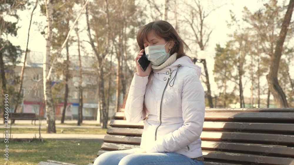 concept health and safety. young woman in medical protective mask is sitting with a smartphone on city street in Europe. Coronavirus protection. tourists on street wear protective mask from viruses.