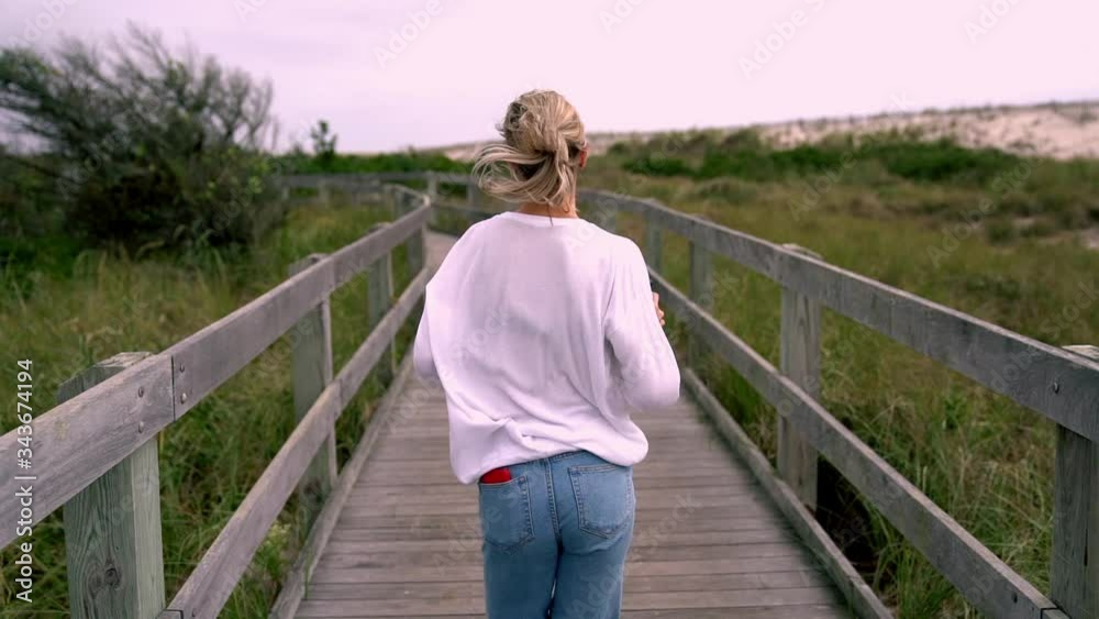 Back view of happy carefree female tourist in jeans enjoying time for travelling during spring holidays running in slow motion on nature park path. Adventures lifestyle, new discoveries and movement
