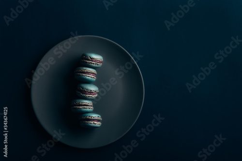 Five blue blueberry macaroons on a blue plate, with a dark blue background 