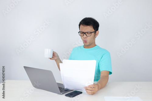 Wow face of Young Asian man shocked what he see in the document when working with laptop. isolated grey background wearing blue shirt.