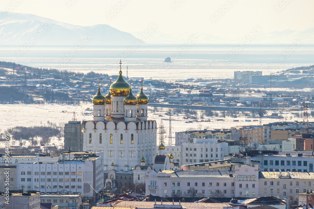 View of the city and a large beautiful church with golden domes. In the distance is the sea bay and mountains. Trinity Cathedral in the city of Magadan. Magadan Region, Siberia, Far East of  Russia.