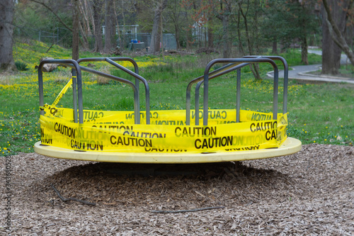 A merry-go-round is wrapped in yellow caution tape warning children and their parents not to use the playground equipment during the COVID-19 or coronavirus epidemic.