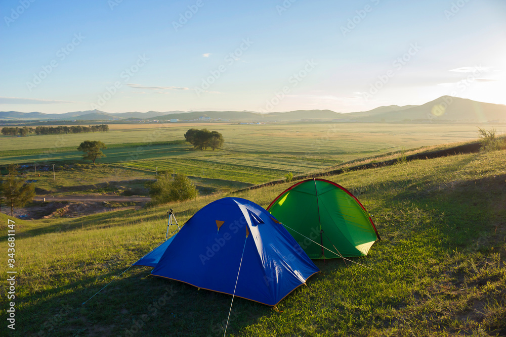 two tents set on a mountain facing grassland