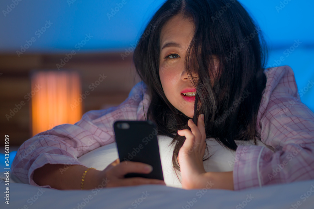 young beautiful and happy sweet Asian Chinese woman and pajamas enjoying online with hand phone in bed at night playing social media at home in internet addiction young beautiful and happy sweet Asian Chinese woman and pajamas enjoying online with hand phone in bed at night playing social media at home in internet addiction