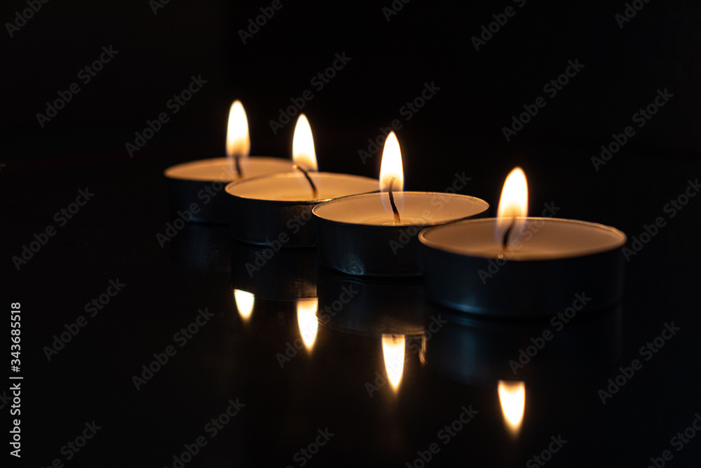 four candles lined up with dark background showing the light of the fire and the reflection in the mirror four candles lined up with dark background showing the light of the fire and the reflection in the mirror