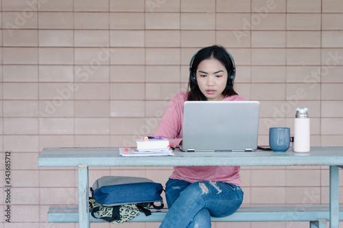 Portrait of a young Asian female adult learner stuying online at home during Coronavirus or COVID-19  pandemic. Businesswoman work with laptop at home in hous corridor and garden photo