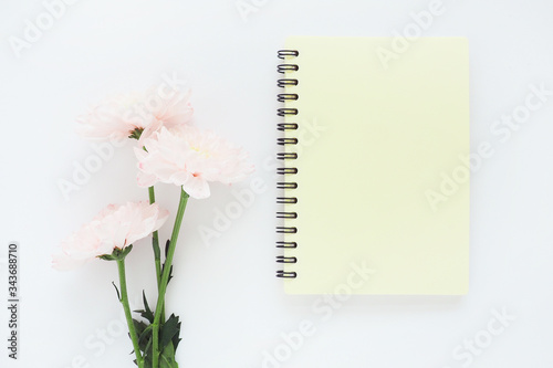 .yellow notebook on a spring and pink chrysanthemum flower on a white table..