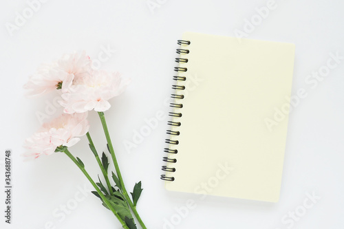 yellow notebook on a spring and three pink chrysanthemum flower on a white table...