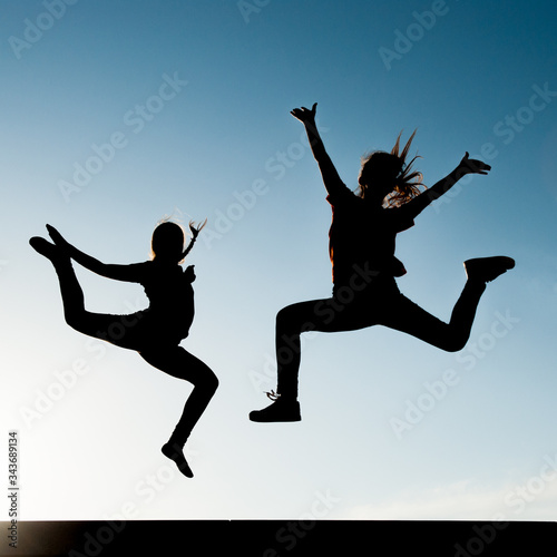 two young active girls jumping on blue sky backgroung outdoor leisure lifestyle