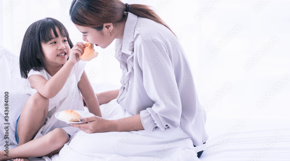 Fototapeta premium Mom and daughter having breakfast on bed