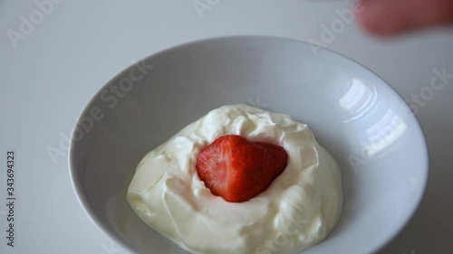 Static frame showing a rotating plate with yogurt while a fresh strawberry falls inside in slow motion photo